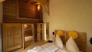 A room with a loft area, wooden walls, a bed with white bedding, and a ceiling light. - Vacation home rehberg14 - historic farm with pond & sauna (Drachselsried)