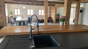 A modern kitchen with a wooden countertop, stainless steel sink, and a dining area with a table and chairs. - Vacation home rehberg14 - historic farm with pond & sauna (Drachselsried)