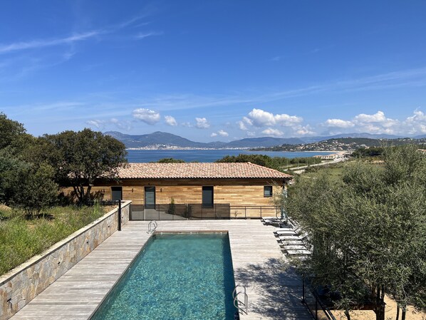 A wooden building with a tiled roof, a swimming pool, and a view of the sea and mountains.