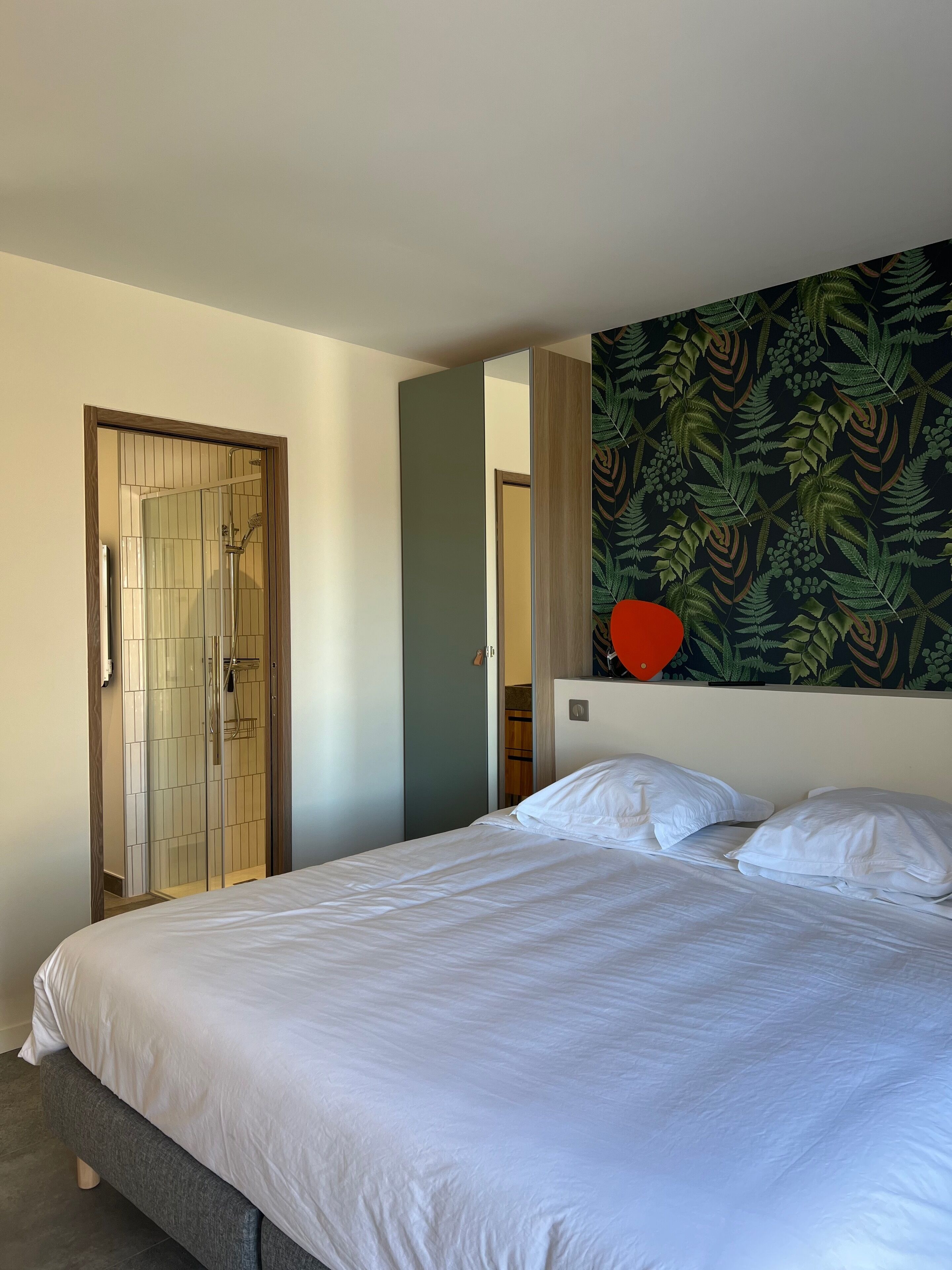 A bedroom with a bed, a wooden door, and a wall with a leafy pattern.