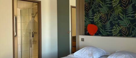 A bedroom with a bed, a wooden door, and a wall with a leafy pattern.
