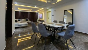 A modern dining area with a round table and chairs, a sofa in the background, and a TV on the wall. - A cosy and contemporary 3 bedroom in Ikoyi (Lagos)