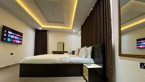 A modern bedroom with a large bed, a bedside table, a flat-screen TV mounted on the wall, and a large mirror. - A cosy and contemporary 3 bedroom in Ikoyi (Lagos)