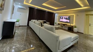 A modern living room with a sectional sofa, a flat-screen TV, and recessed ceiling lighting. - A cosy and contemporary 3 bedroom in Ikoyi (Lagos)