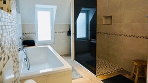Un bany modern amb banyera, zona de dutxa i una finestra gran que aporta llum natural.