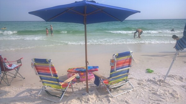 Una playa con dos sillas de playa a rayas, una mesa y una sombrilla azul.