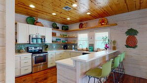 A modern kitchen with wooden cabinets, a stainless steel oven, a microwave, and a bar area with green bar stools. - Near Beach, Balcony Overlooking Private Pond, Private Pool (Port Aransas)