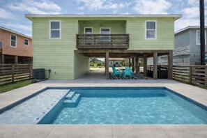 Uma casa de dois andares com piscina no quintal, um alpendre coberto com mobiliário de exterior e uma cerca de madeira.