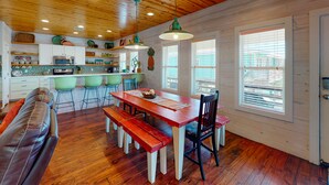 A wooden interior with a dining table, benches, and a kitchen area with bar stools. - Near Beach, Balcony Overlooking Private Pond, Private Pool (Port Aransas)