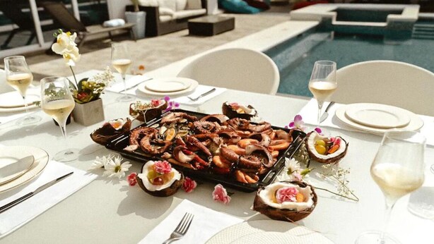 A dining table set for a meal with seafood, wine glasses, and a poolside view. - Luxury Villa in a Private Area (Punta Cana)