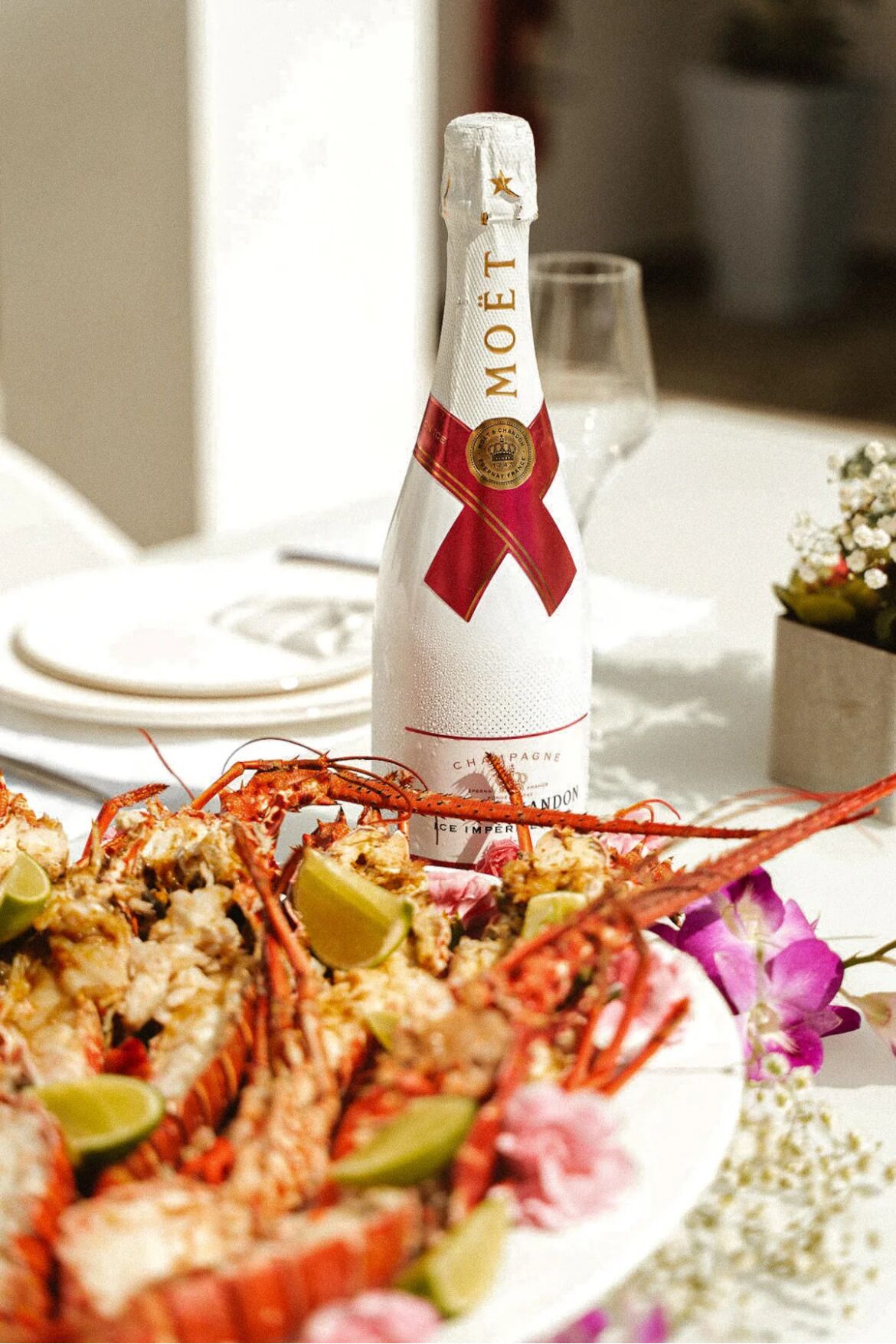 Une bouteille de champagne Moët, un plat de homard et un verre de vin sur une table.
