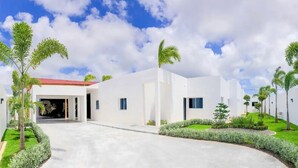 A modern building with a red roof, white walls, and a paved courtyard with palm trees and shrubs. - Luxury Villa in a Private Area (Punta Cana)