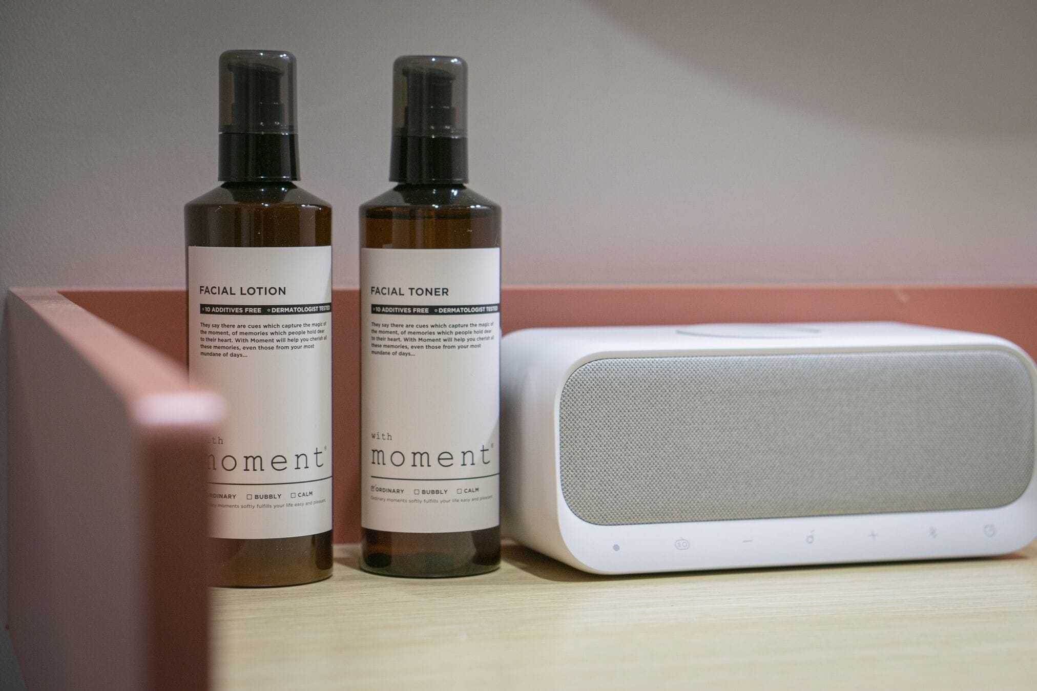Two bottles of facial lotion and a white speaker on a wooden surface.