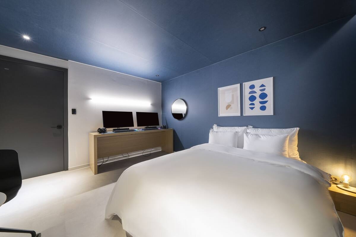 A modern hotel room with a large bed, a desk with a computer, and a wall-mounted TV.