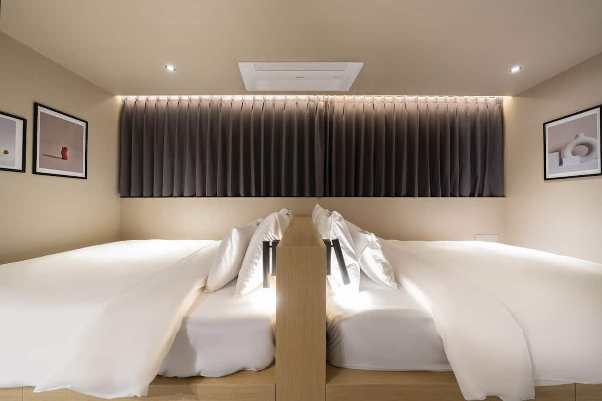 A hotel room with a large bed, a ceiling-mounted air conditioner, and a curtain.