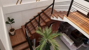 En modern trappa med trästeg och svarta räcken, som leder upp till en liten plattform med en vadderad bänk och en krukväxt.