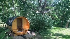 Una struttura cilindrica in legno con una porta aperta, immersa in una zona boschiva.