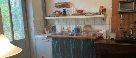 A kitchen with a wooden table and chairs, a window, and a microwave on a wooden shelf.