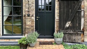 A brick building with a black front door, large windows, and a wooden gate. - Vacation apartment Beelitz - Barn Zauchwitz (Beelitz)