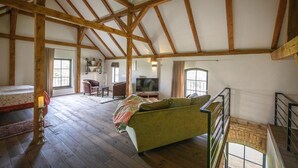A spacious loft with exposed wooden beams, a green sofa, a television, and a staircase. - Vacation apartment Beelitz - Barn Zauchwitz (Beelitz)