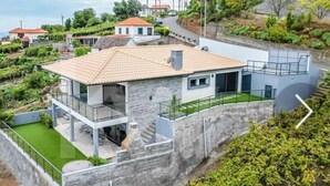 A modern house with a stone facade, a tiled roof, and a balcony with glass railings. - House - Sleeps 3, Free Parking, Garden & Jacuzzi (Calheta)