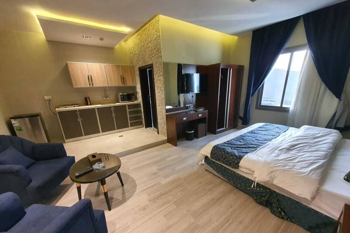 Ein Hotelzimmer mit Bett, Schreibtisch, Stuhl, kleinem Tisch und einer Küchenzeile.