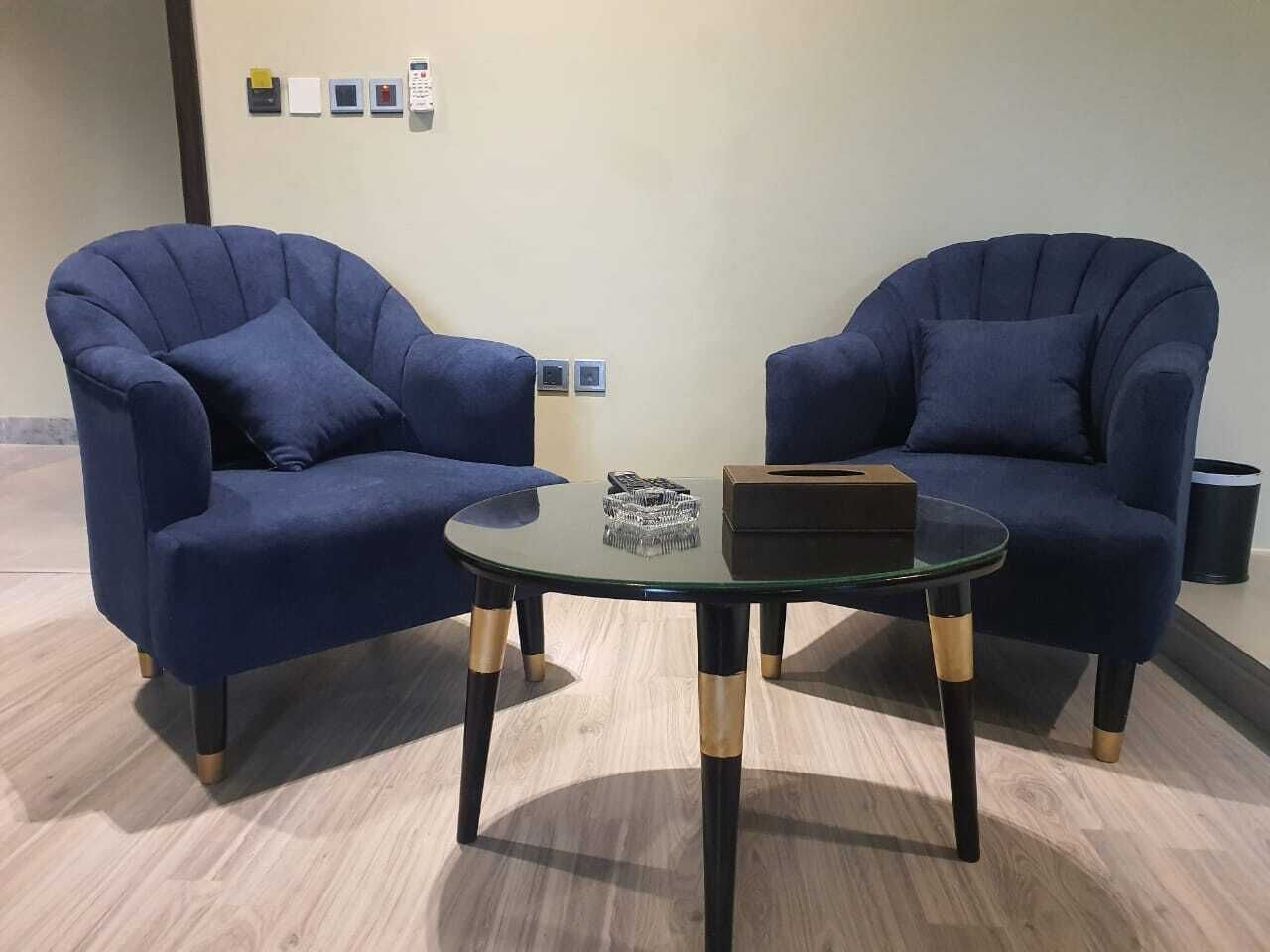 Two blue armchairs facing each other with a glass table in between, featuring a small decorative item and a box on the table.