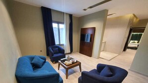 A modern living room with two blue armchairs, a coffee table, and a flat-screen TV mounted on a wooden panel. - Alfadel Residential Units (Al Baha)