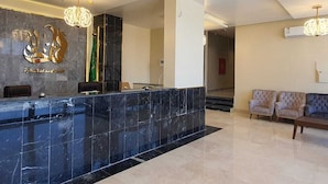A hotel reception area with a marble reception desk, two sofas, and a chandelier. - Alfadel Residential Units (Al Baha)