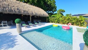 A swimming pool with lounge chairs and a thatched-roof structure. - POSHPADZ Presents Villa Tranquila- Private Pool & Tiki Close to Beach Sleeps 10 (Jupiter)
