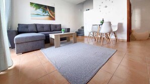 Un salon moderne avec un canapé gris, une table basse et un coin repas avec des chaises blanches.