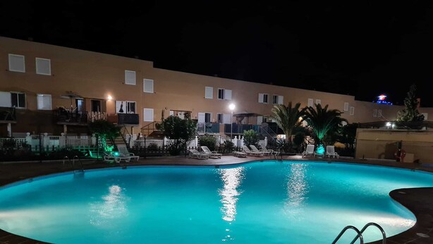 Une piscine avec une plage en briques, entourée d’un bâtiment doté de nombreux balcons et d’un éclairage extérieur soigné.