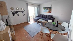 Un salon moderne avec un canapé, une table à manger et des chaises. Un grand planisphère est accroché au mur, ainsi qu’un tableau représentant une scène de plage.
