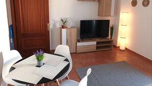 Un espace de vie compact comprenant une porte en bois, un téléviseur posé sur un meuble en bois, un petit placard et une table avec des chaises.