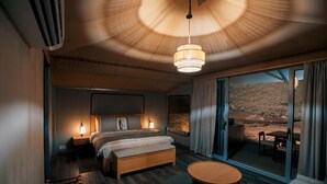 A modern hotel room with a large bed, a round table, and a view of a rocky landscape through the glass door. - Moon Retreat by Sharjah Collection (Mleiha)