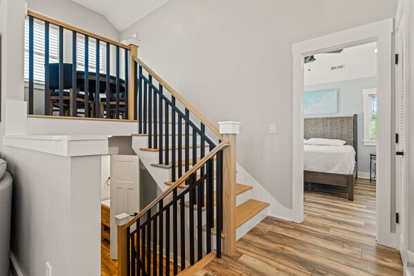 A staircase with wooden steps and black railings leading to a bedroom with a bed and a nightstand. - Landon Sea: Private Pool, Hot Tub, Dog-Friendly (Corolla)