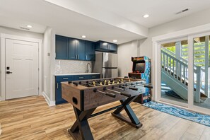 A modern kitchen with blue cabinets, a stainless steel refrigerator, and a foosball table. - Landon Sea: Private Pool, Hot Tub, Dog-Friendly (Corolla)