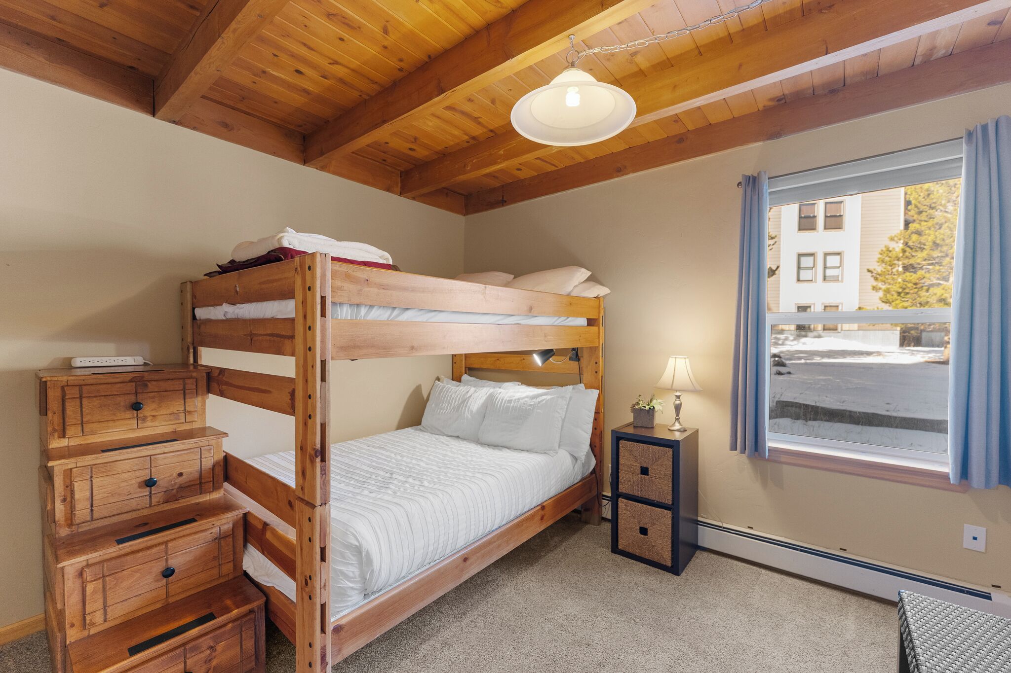 A bunk bed room with a wooden dresser and a nightstand.