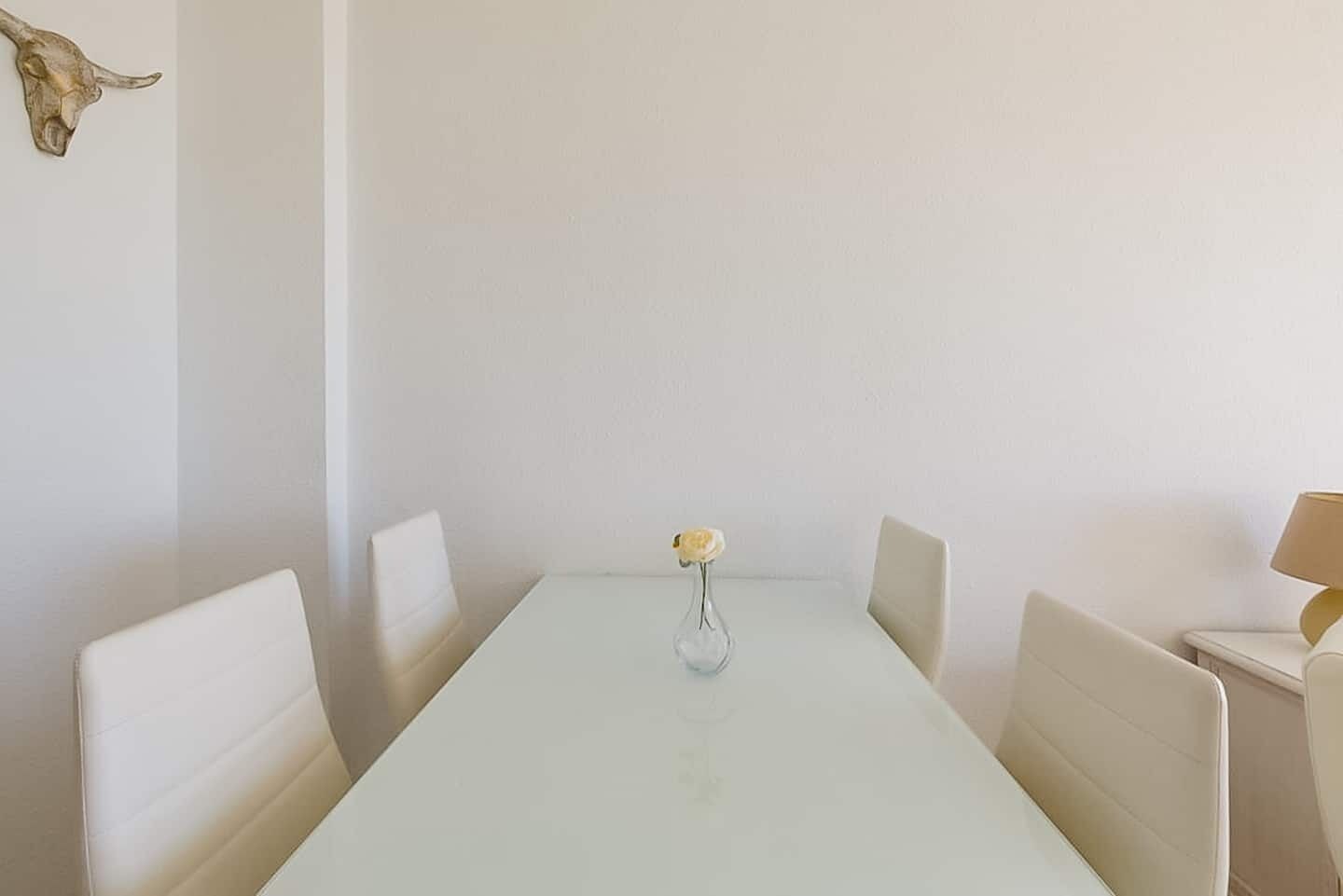 Une table à manger avec quatre chaises, un vase contenant une seule fleur et un crâne de vache accroché au mur.