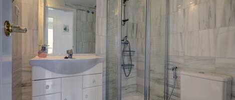 A bathroom with a glass-enclosed shower, a white sink, and a toilet.