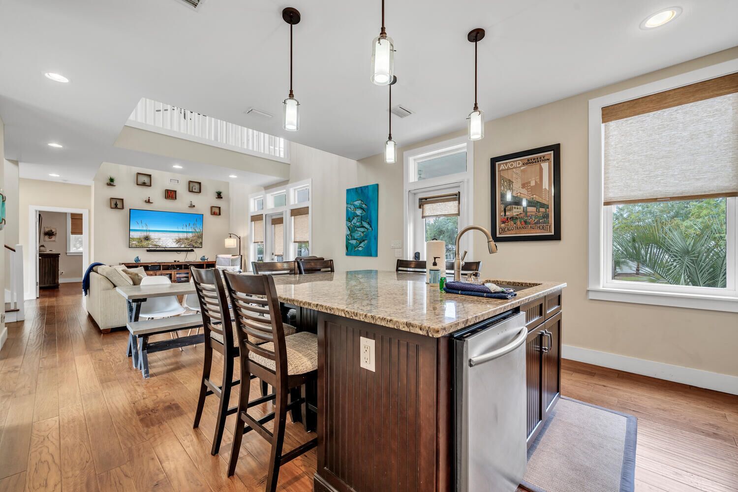 A modern kitchen with a central island, bar stools, pendant lighting, and a large window.