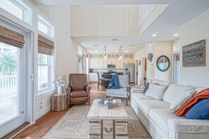 Relax in this spacious living area with a high ceiling and large windows, featuring a sofa, coffee table, and armchair.