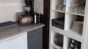 Een keuken met een koffiezetapparaat, magnetron en planken met servies en pannen.