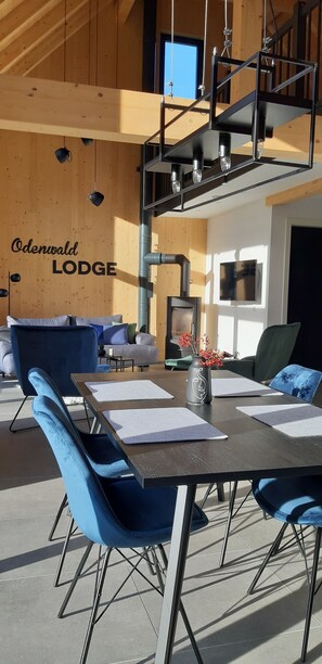 L’intérieur d’un chalet moderne comprend un coin repas, des chaises bleues, une table avec des sets de table, une cheminée et un téléviseur fixé au mur.