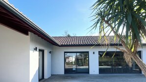 Une maison moderne dotée d’une terrasse en bois, d’une piscine et de grandes portes vitrées.