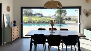 Un espace repas doté d’une grande fenêtre donnant sur une piscine et offrant une vue sur un quartier résidentiel.