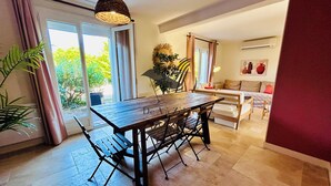 A dining area with a wooden table and chairs, a hanging light fixture, and a view of the outdoors through a glass door.