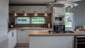 A modern kitchen with white cabinets, a large island with a stove, a microwave, and a window overlooking a garden. - Maple Lodge | sleeps 6 - Hot Tub, Dog Friendly - 5* Visit England (Pickering)