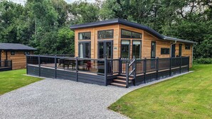 A modern wooden cabin with a deck, surrounded by a gravel path and lush greenery. - Maple Lodge | sleeps 6 - Hot Tub, Dog Friendly - 5* Visit England (Pickering)