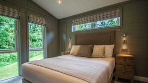 A bedroom with a large bed, two bedside tables, and a window with a view of greenery. - Maple Lodge | sleeps 6 - Hot Tub, Dog Friendly - 5* Visit England (Pickering)